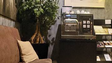 A cozy room with a brown sofa, a coffee machine, a potted plant, and a framed picture on the wall.