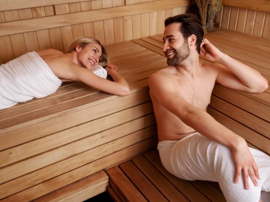 A couple relaxing in a wooden sauna with benches.