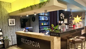 Un espace d’accueil avec un comptoir en marbre portant l’inscription « RÉCEPTION », une horloge, un bar avec des étagères remplies de boissons et deux tabourets de bar.