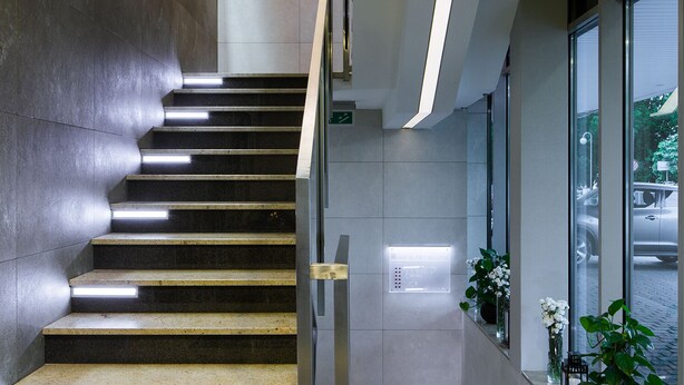 Un escalier moderne avec une rampe en métal, menant à un palier doté d’une porte en verre.