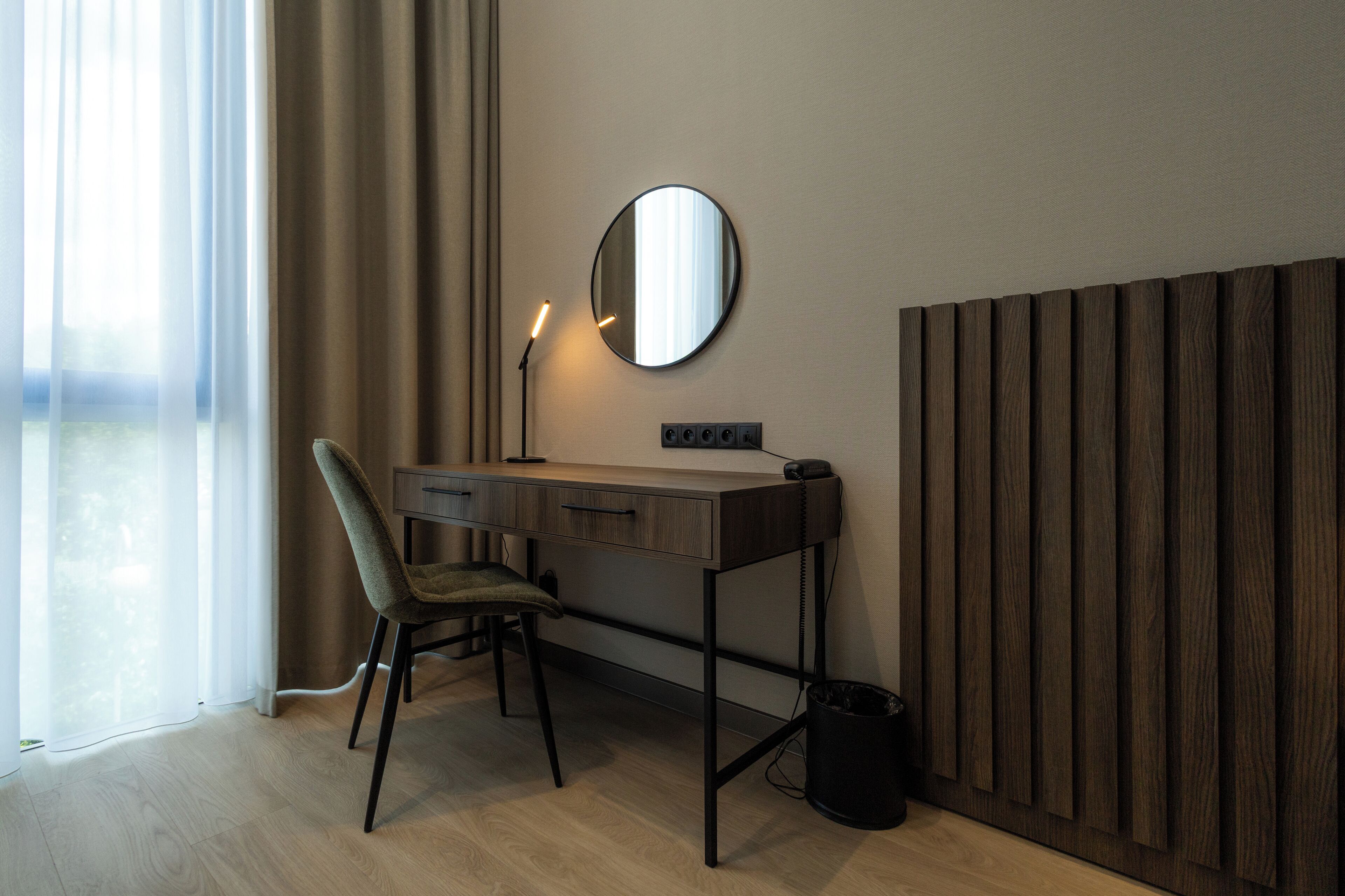 A modern workspace with a desk, chair, and a round mirror on the wall.