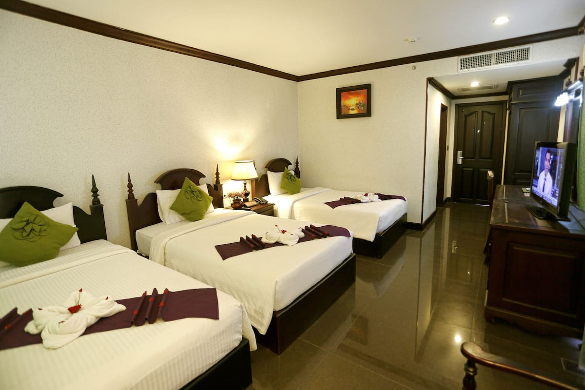 A hotel room with two beds, each with neatly made pillows and towels. There is a television on a wooden cabinet and a painting on the wall.