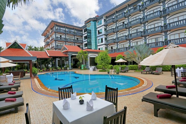 A hotel with a swimming pool, outdoor seating, and a multi-story building with balconies. - Lucky Angkor Hotel & Spa (Siem Reap)