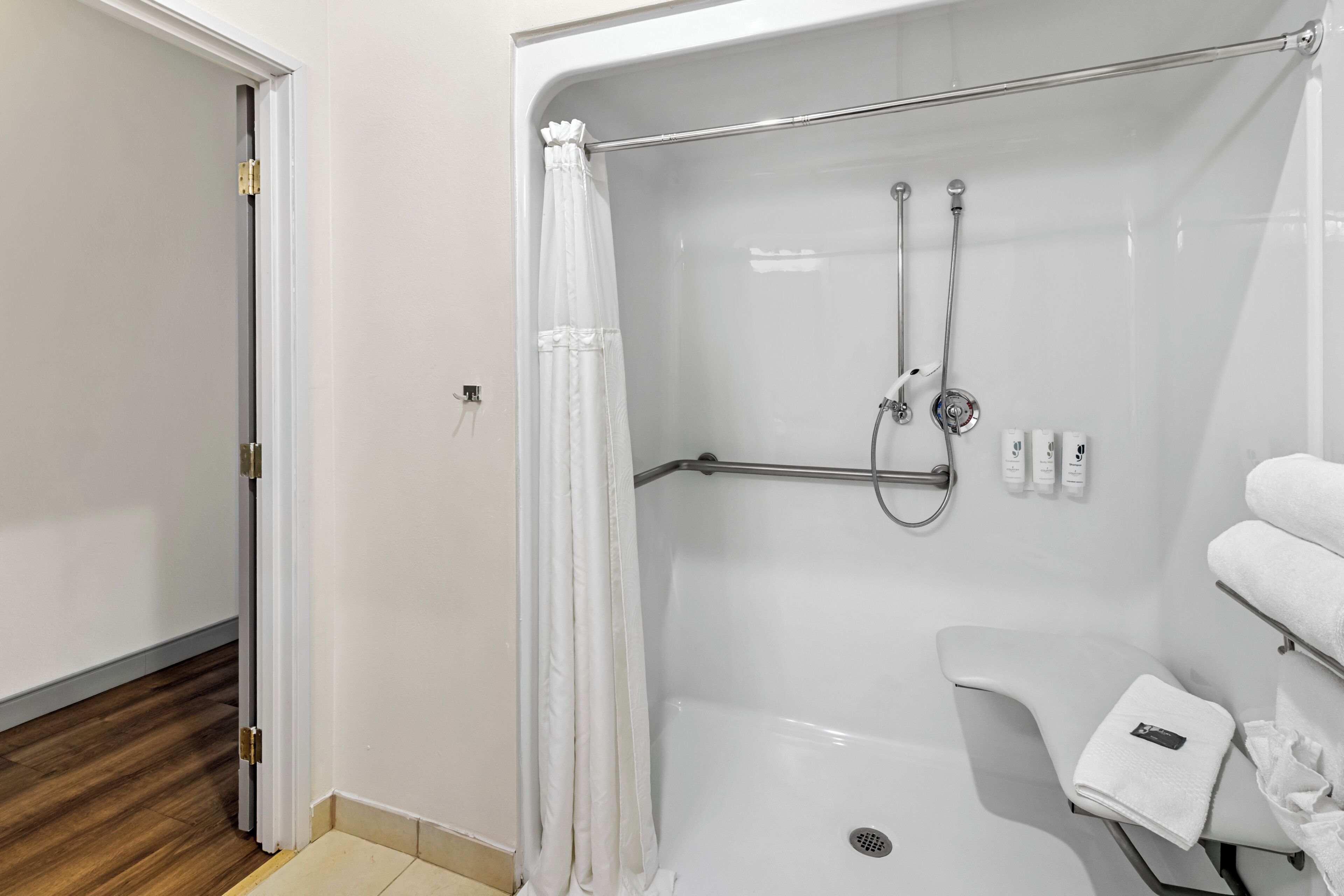 Et moderne bruseområde med glasvægge, brusehoved i håndtagshøjde, et håndklædetørrestativ og et toilet.