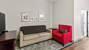 A living room with a beige sofa, a red armchair, a TV on a stand, and framed pictures on the wall.