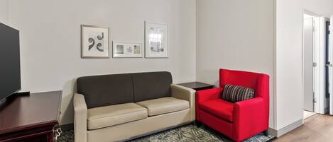 A living room with a beige sofa, a red armchair, a TV on a stand, and framed pictures on the wall.