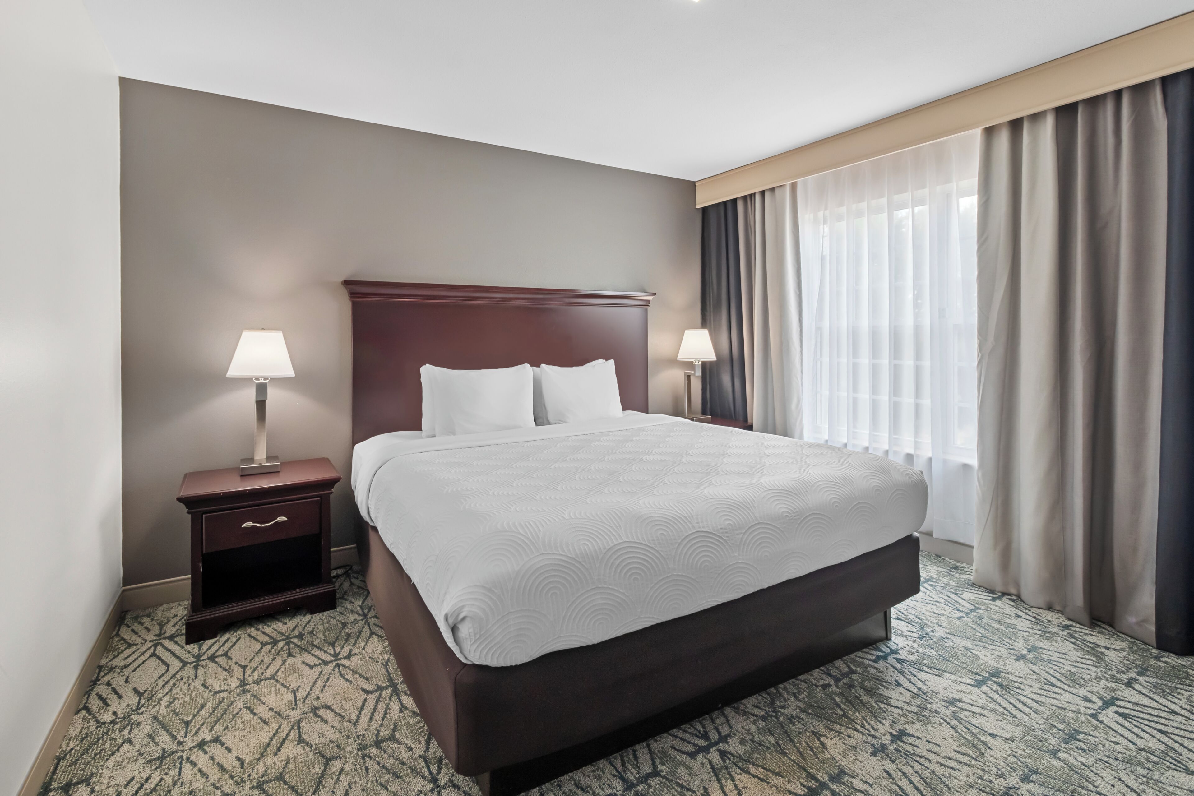 A hotel room with a large bed, two bedside tables, a nightstand, and a window with curtains.
