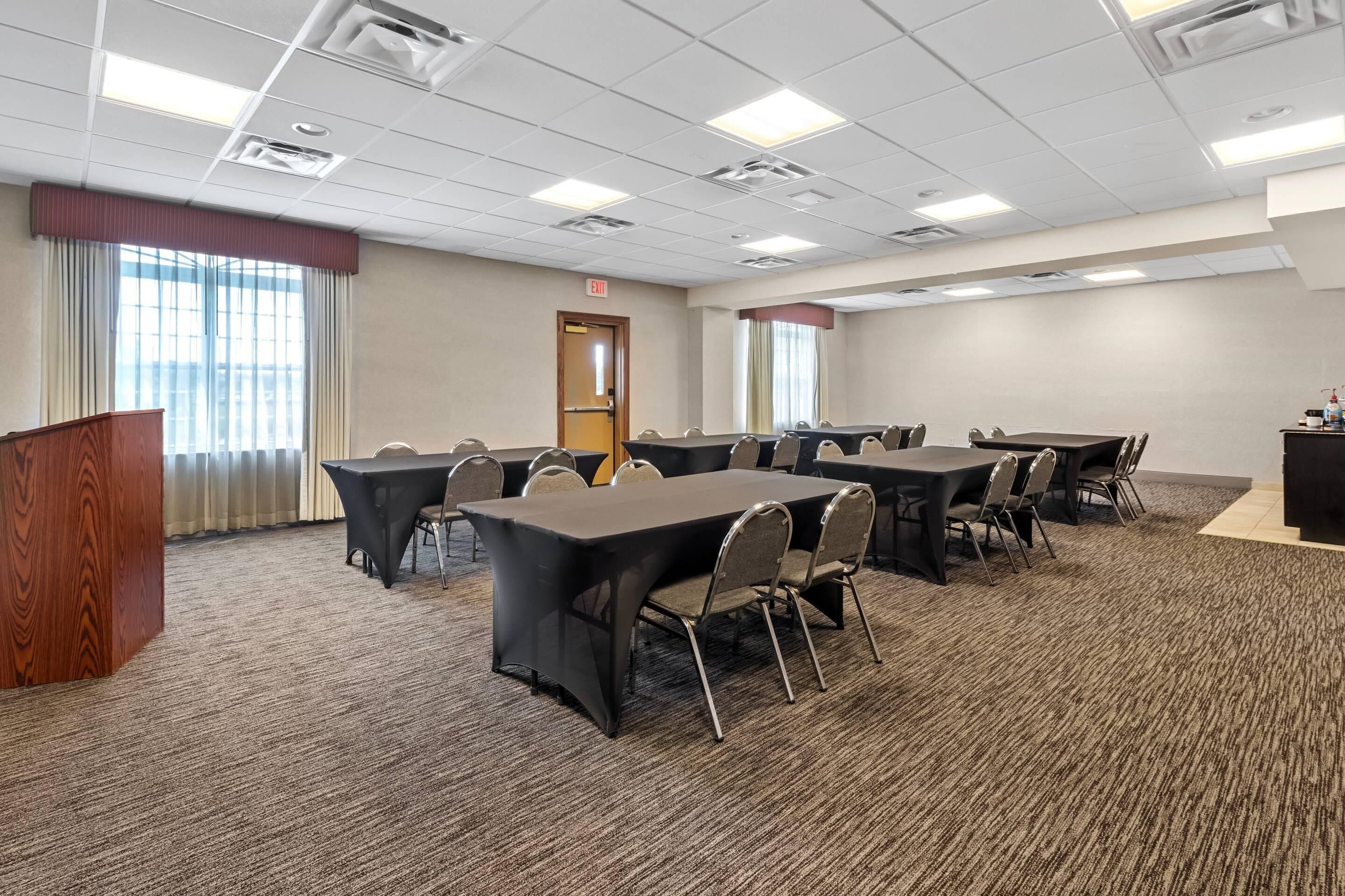 A conference room with a podium, multiple tables, chairs, and a carpeted floor.