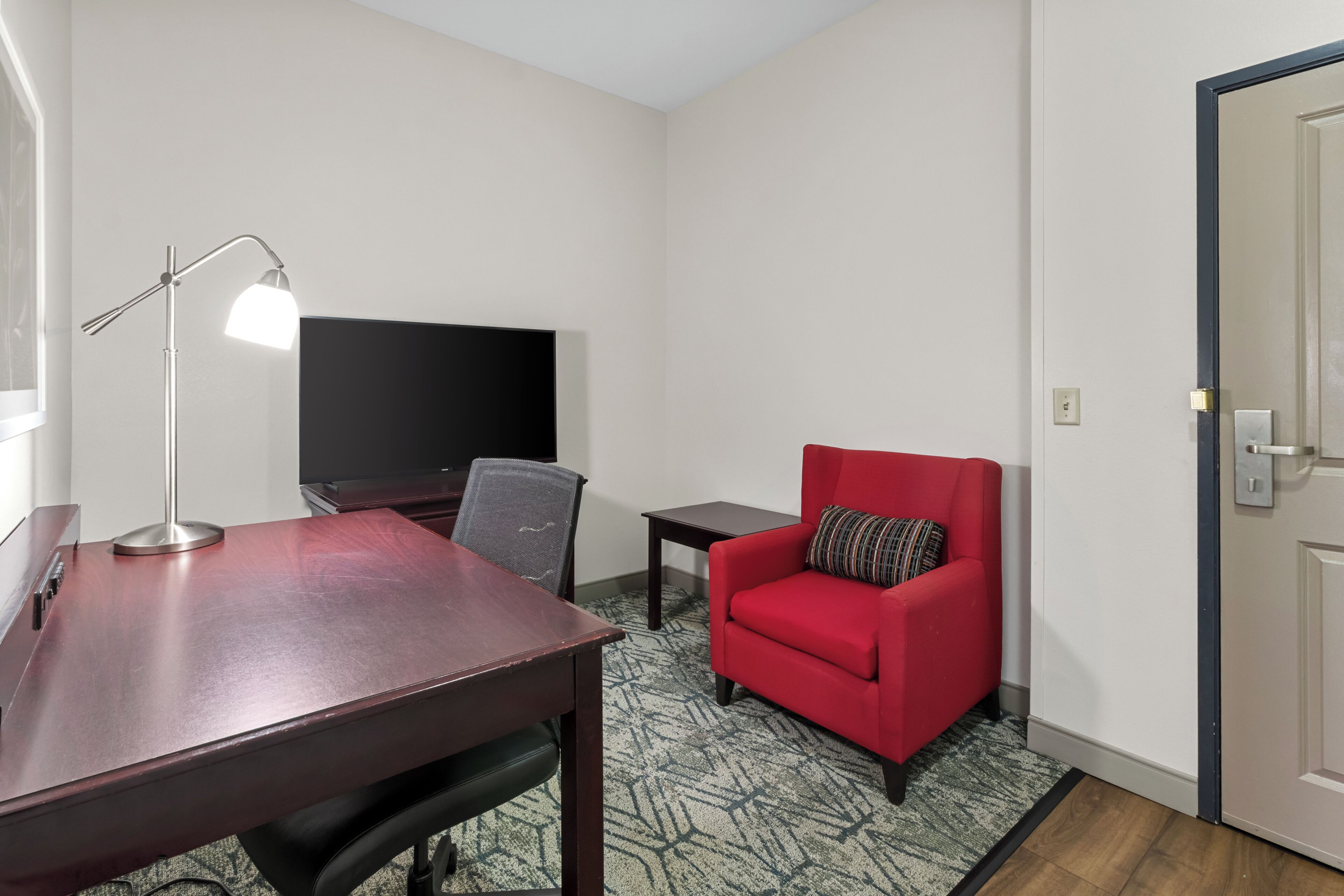 Una habitación de hotel con escritorio, una silla, televisor y sofá rojo.