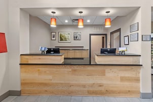 Un mostrador de recepción con dos computadoras, paneles de madera e iluminación colgante.