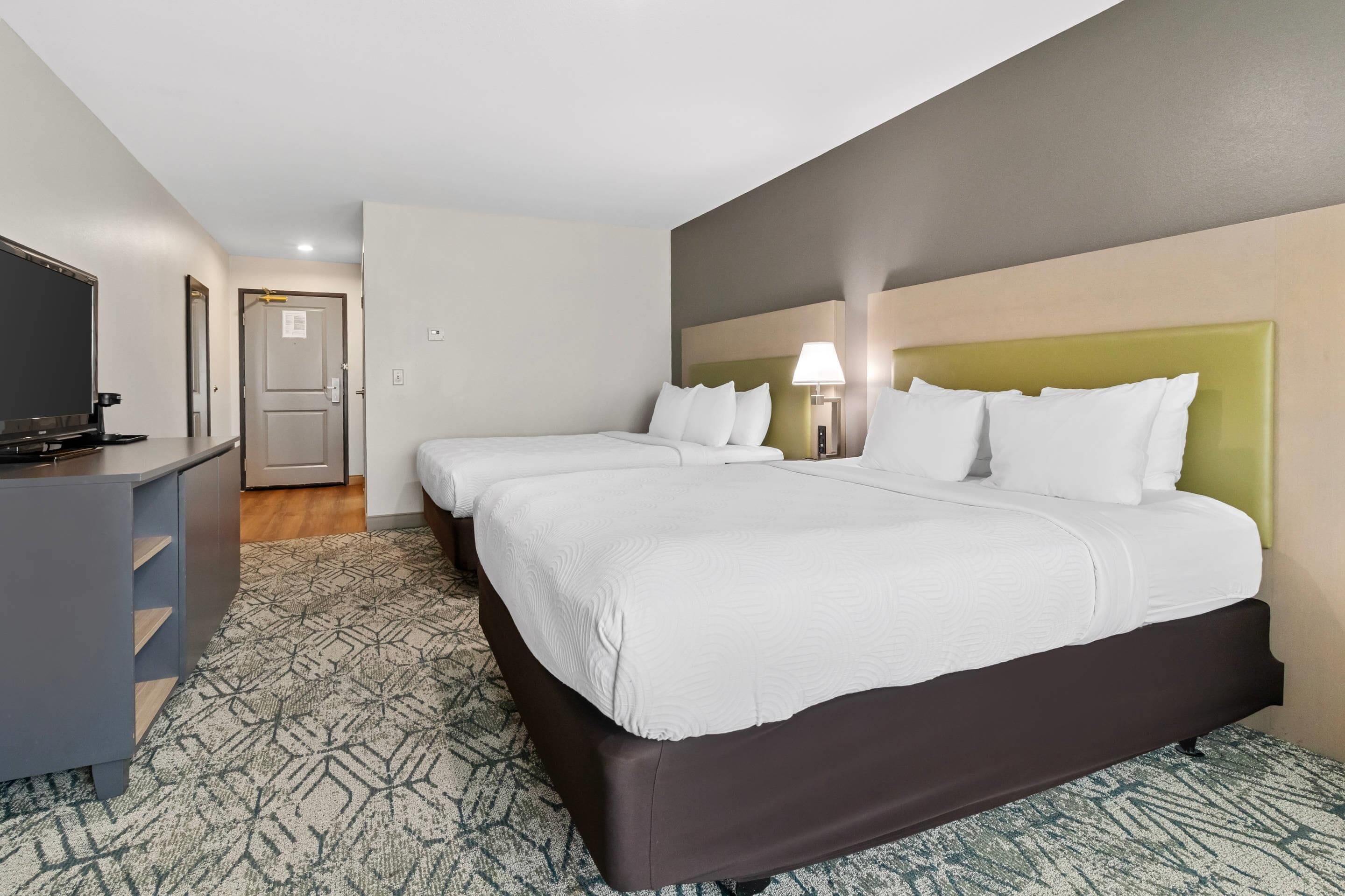 A hotel room with a large bed, a desk with a flat-screen TV, and a patterned carpet.