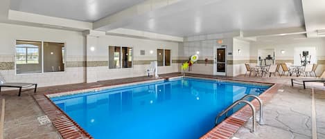 An indoor swimming pool with a clear blue water, tiled walls, and a brick border.