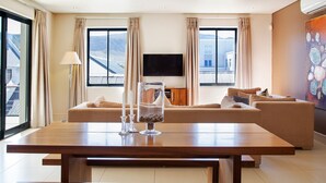 Un soggiorno moderno con un grande tavolo in legno, divani beige, una TV a schermo piatto e ampie finestre con tende.