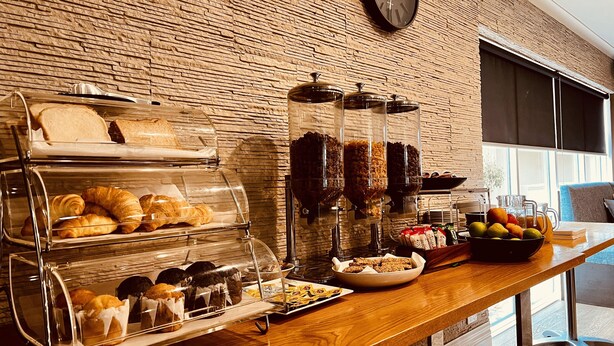 A breakfast buffet with various pastries and fruits, a clock on the wall, and a window with blinds.
