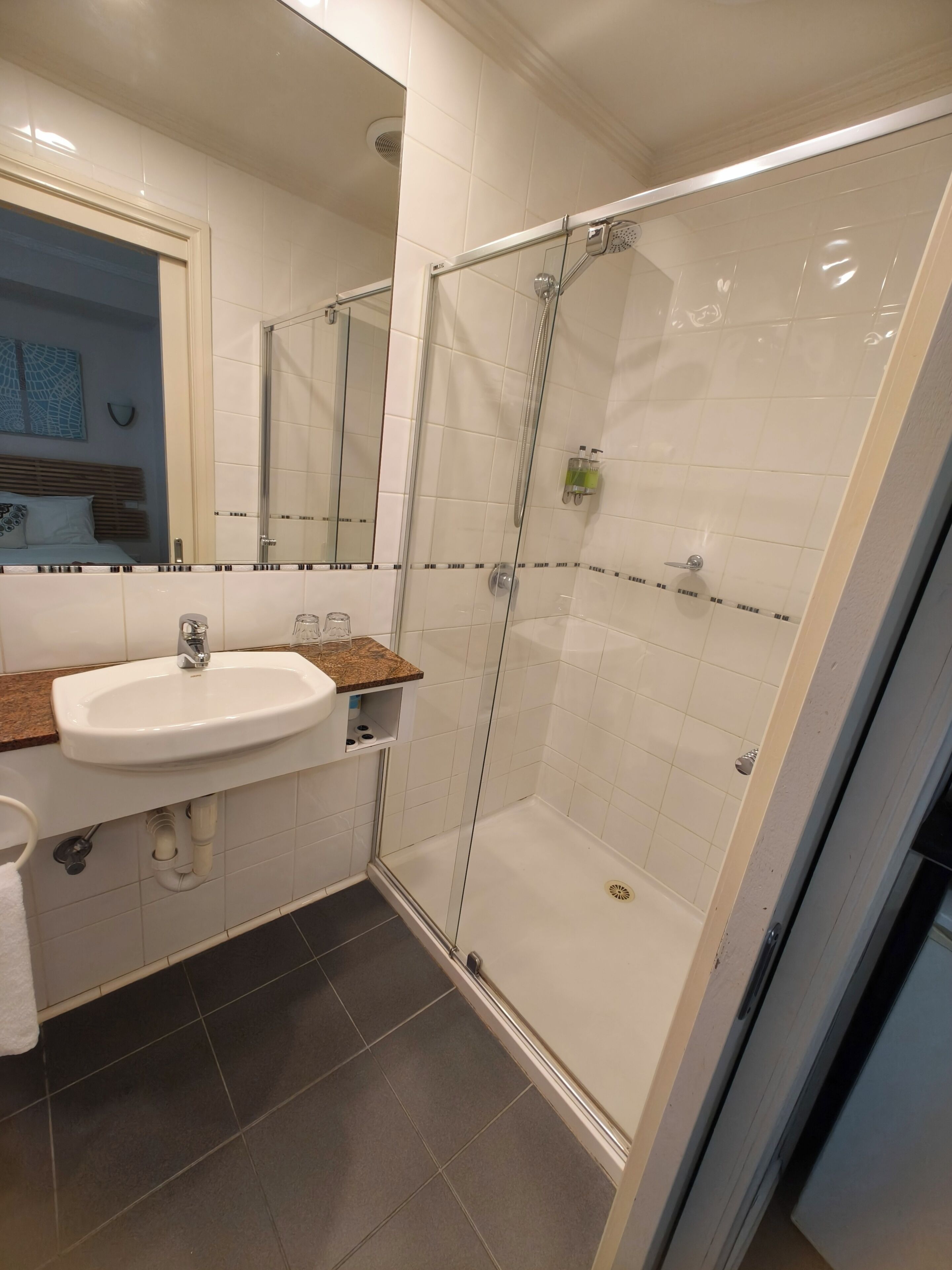 Een badkamer met een witte wastafel, een douchecabine van glas en een spiegel.