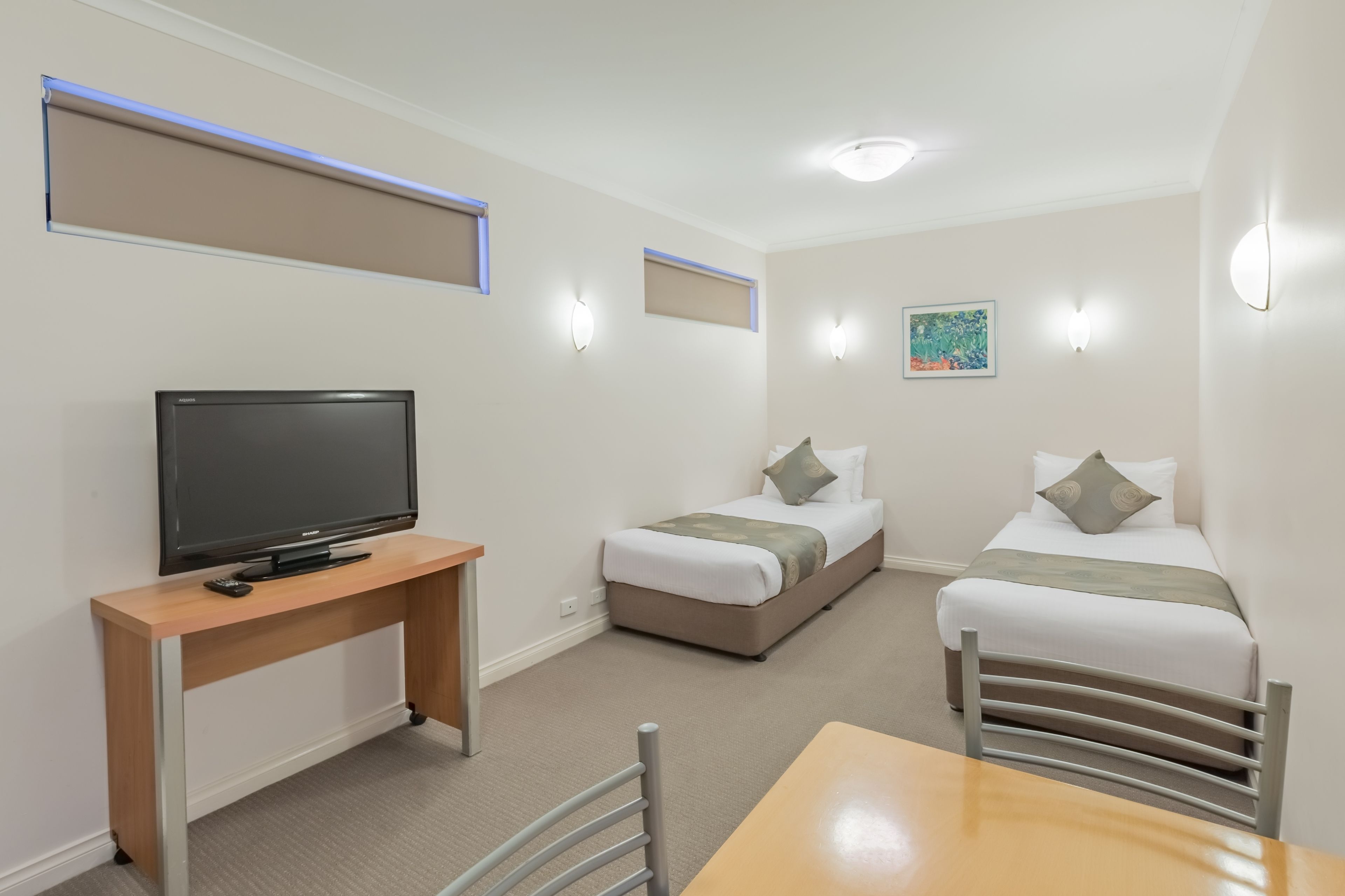 A hotel room with a TV, two beds, a desk, and a table.