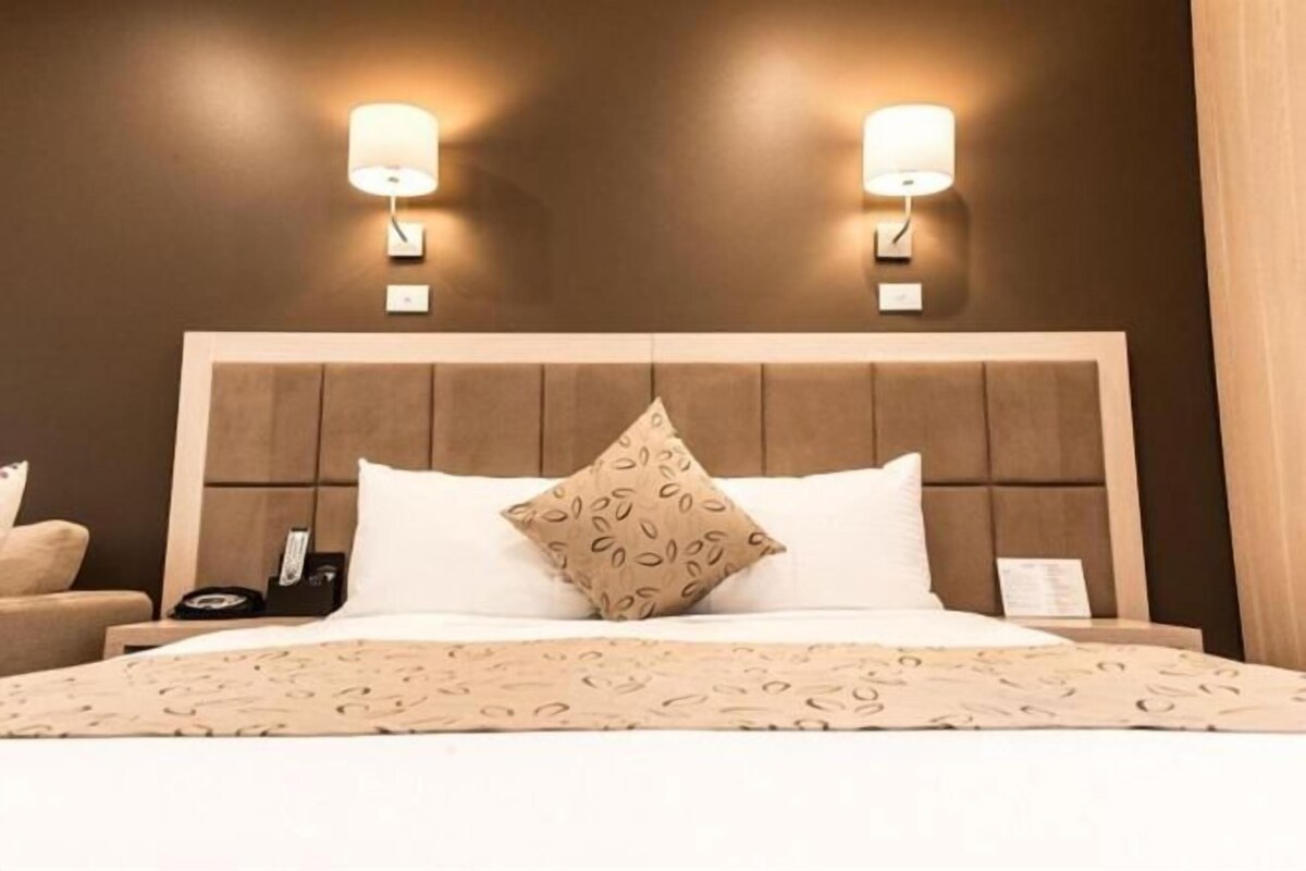 A hotel room with a large bed, two wall-mounted lamps, and a headboard with a padded design.