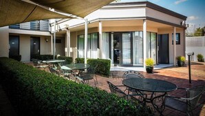 An outdoor patio area with tables and chairs, a covered seating area, and potted plants.
