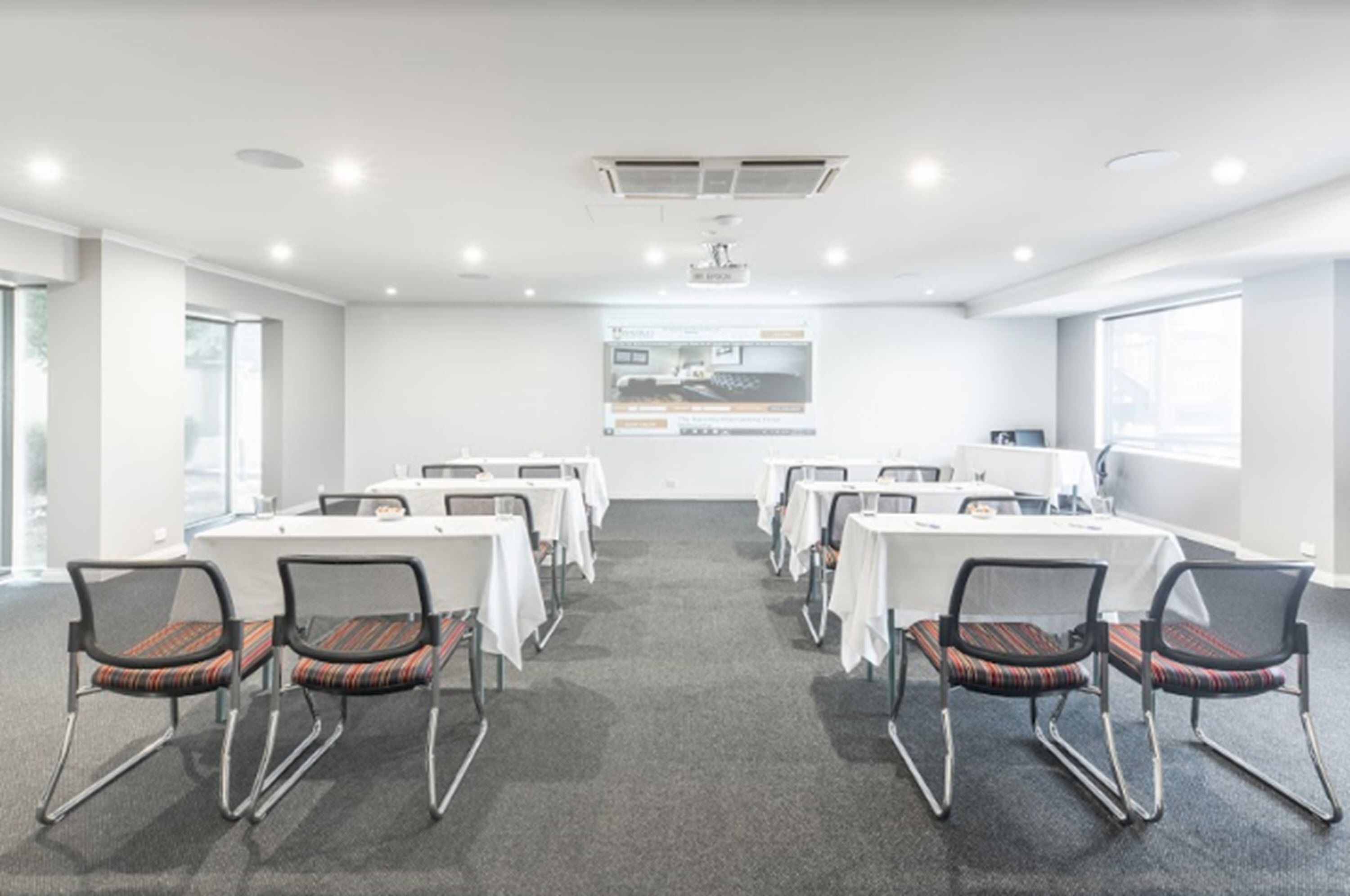 A conference room with tables and chairs, a projector screen, and large windows.