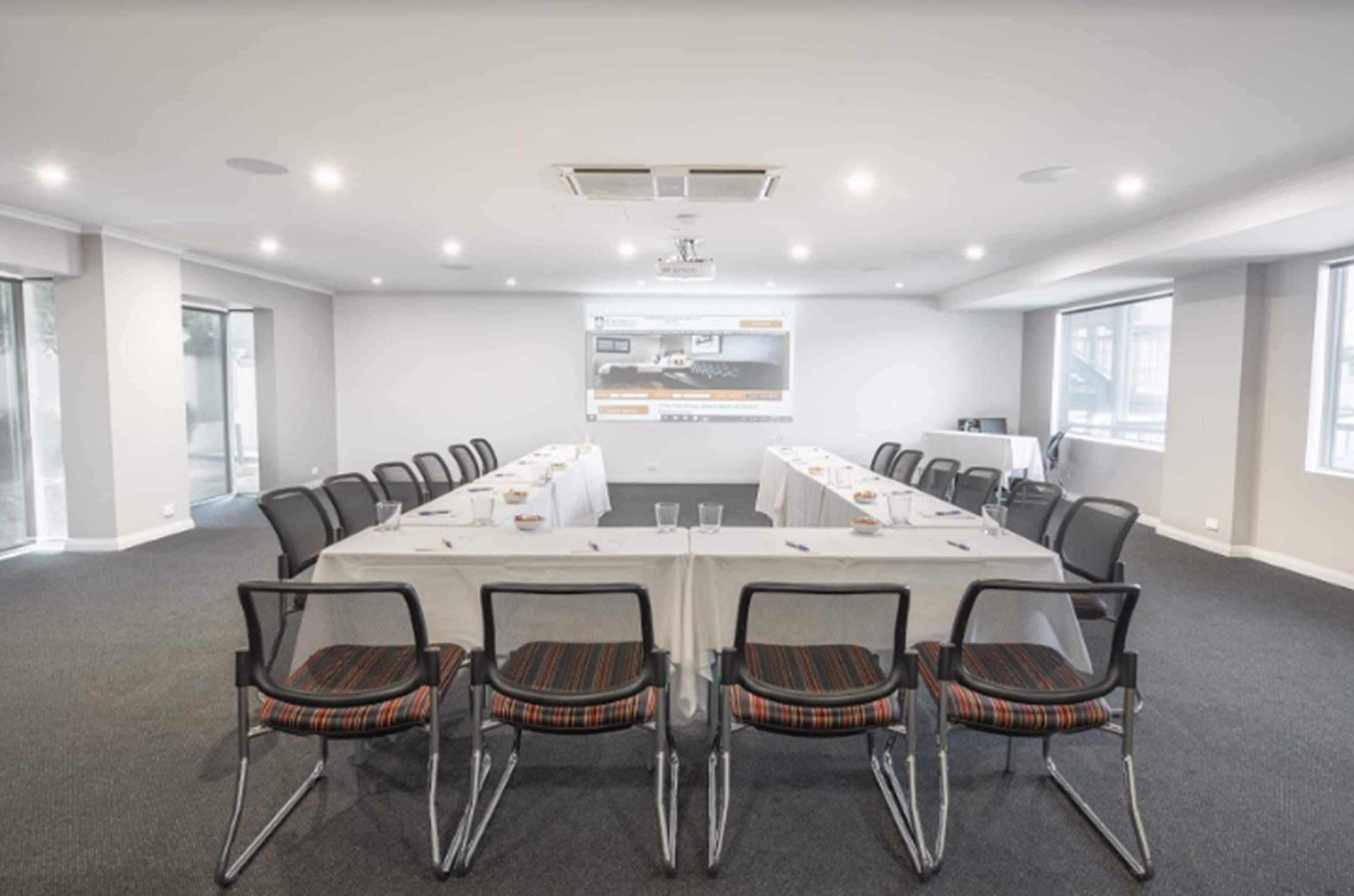 A conference room with a long table, chairs, and a projector screen.
