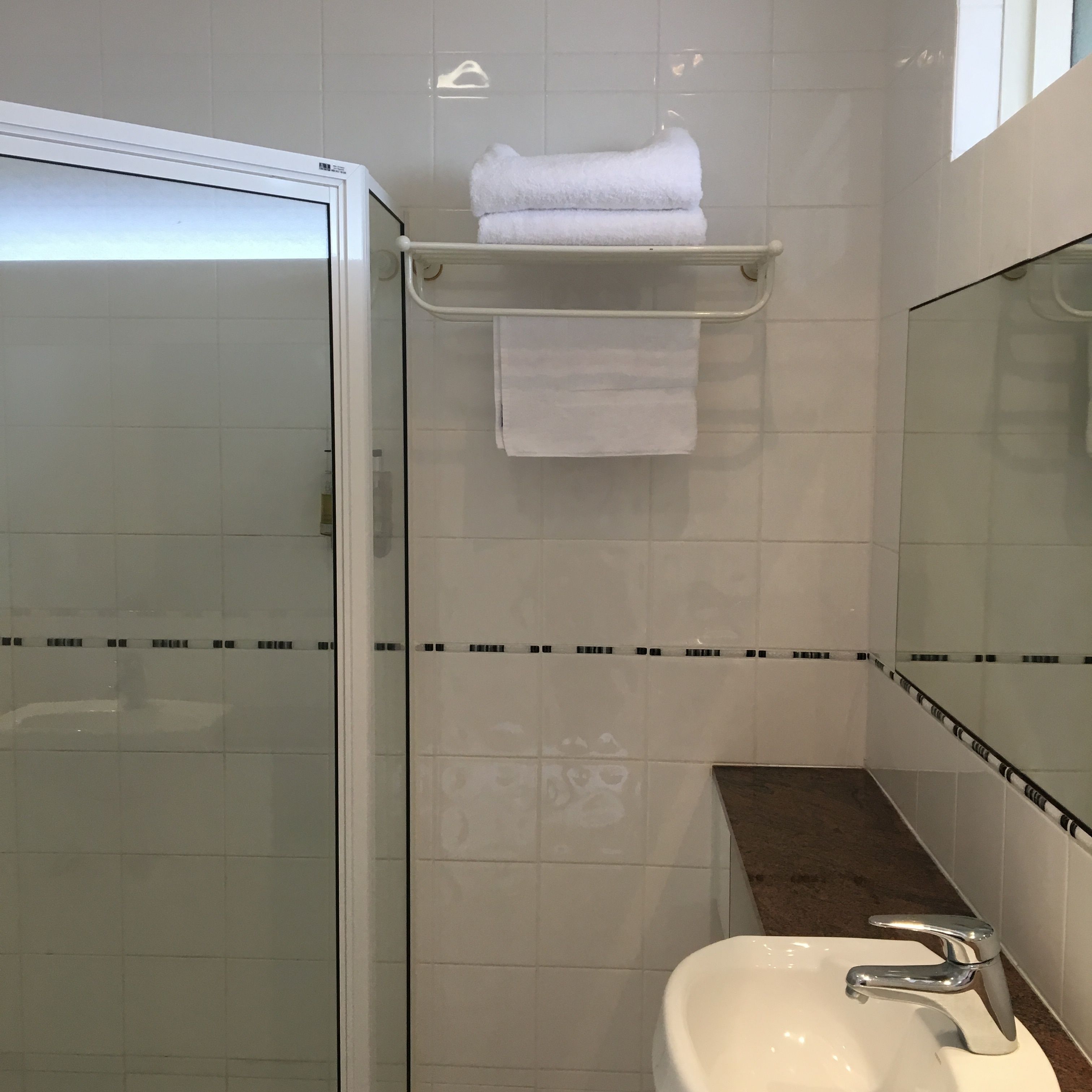 A bathroom with a glass shower enclosure, a white sink with a chrome faucet, and a towel rack with folded towels.