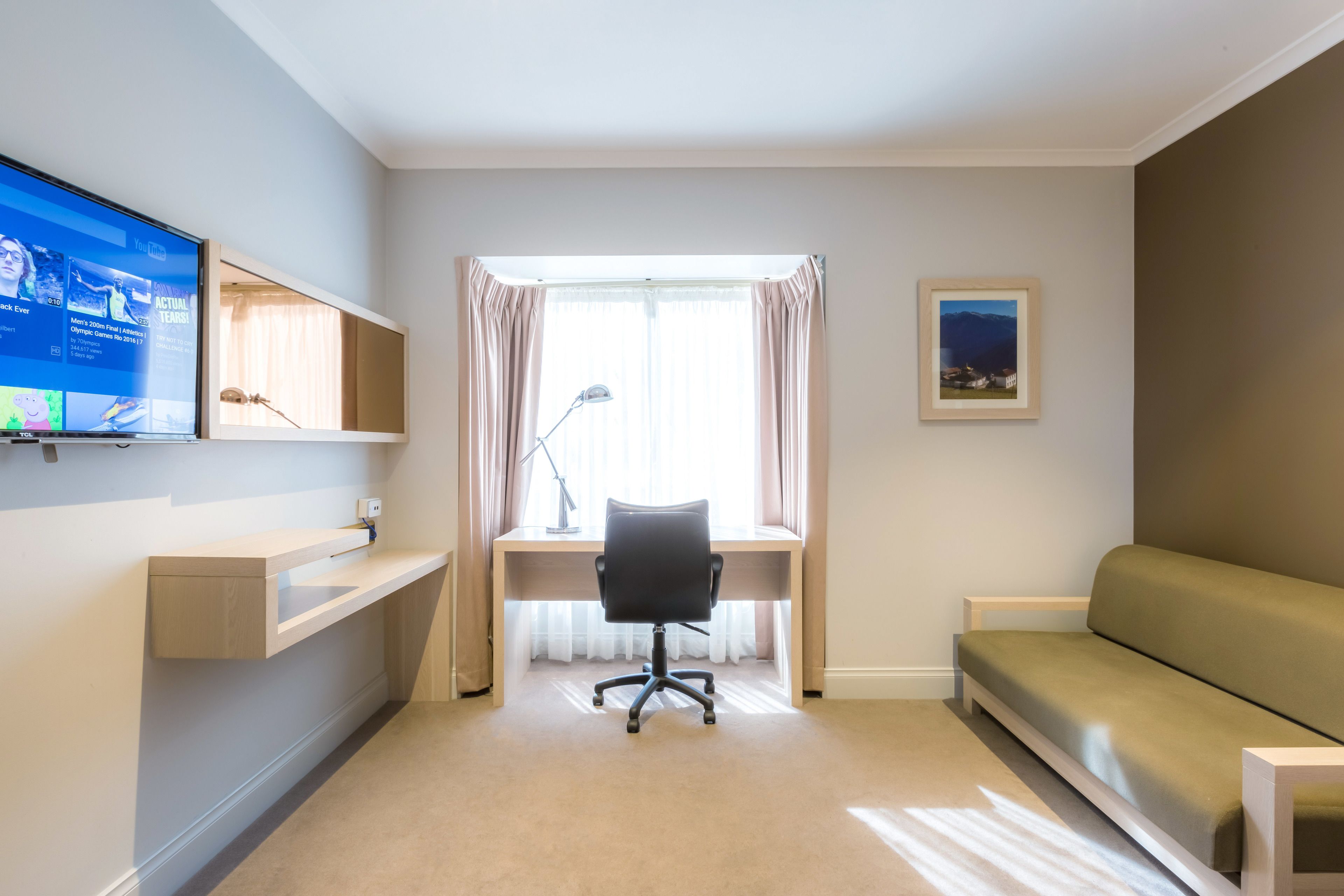 A modern room with a desk, a chair, a sofa, a TV, and a window with curtains.