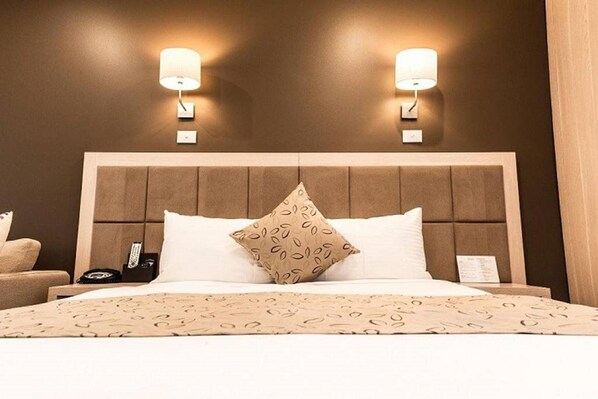 Een hotelkamer met een groot bed, twee wandlampen, een hoofdeinde en een nachtkastje met een telefoon.