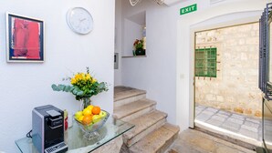 A reception area with a glass table holding a vase of flowers and a bowl of fruit, a clock, and a framed artwork on the wall. - Villa Flores - Apartments (Dubrovnik)