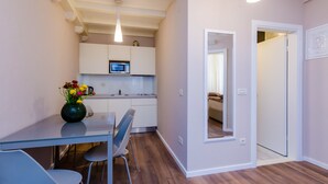 A modern kitchen with white cabinets, a microwave, and a dining area with a glass table and chairs. - Villa Flores - Apartments (Dubrovnik)