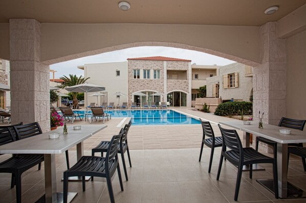 A poolside area with outdoor seating and a view of a building with a stone facade and a tiled roof. - Maravel Star Art Hotel (Rethymno)