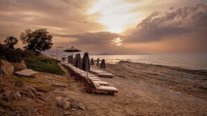 Una playa con tumbonas y sombrillas, una torre de socorristas y vista al mar al atardecer.