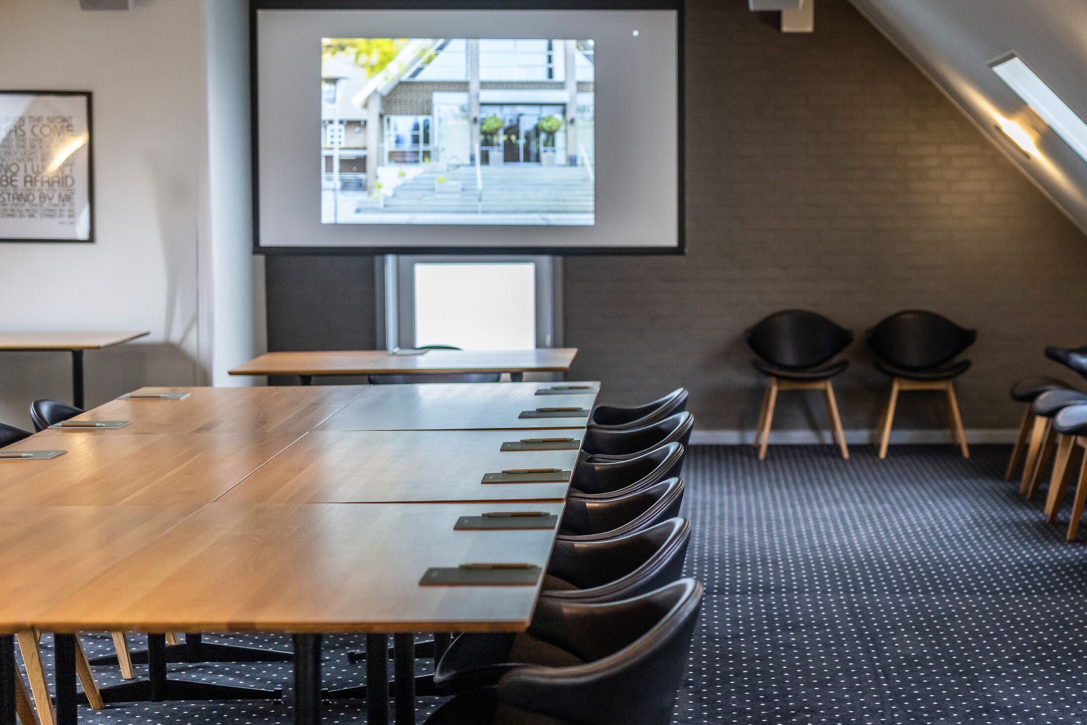 A conference room with a long table, chairs, a projector screen, and a view of the outside.