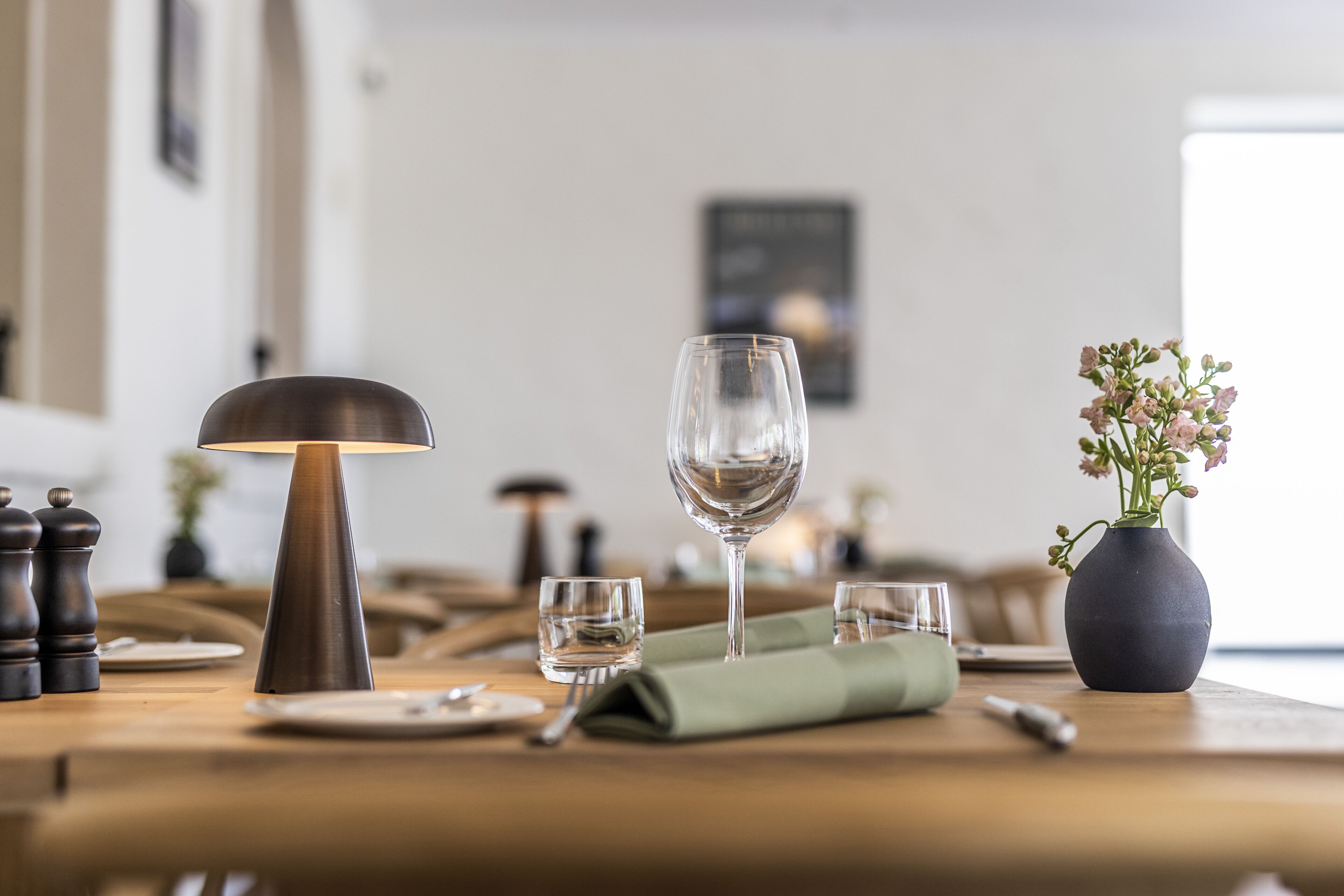 A dining table with a lamp, wine glass, and a vase with flowers.