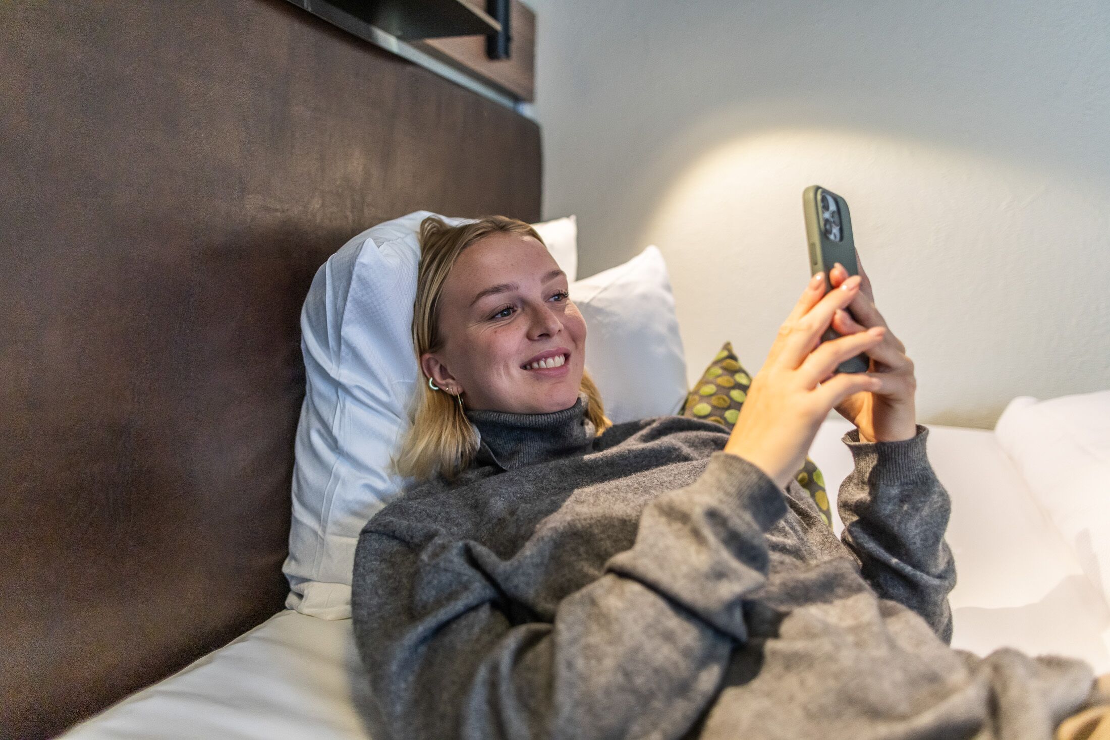 Iemand ligt op een bed met een smartphone, een kussen en een hoofdbord.