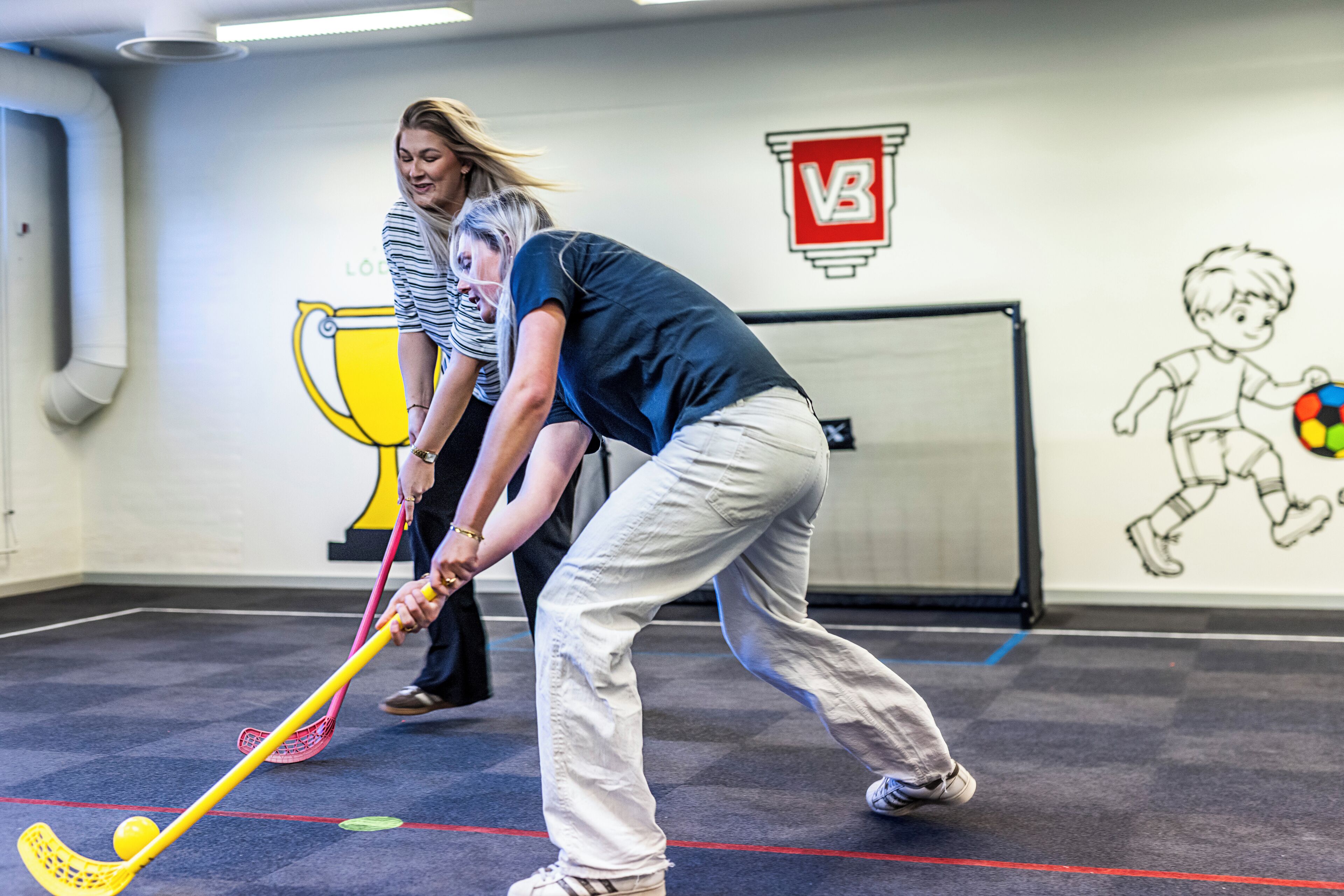 An indoor sports facility with a hockey stick, a trophy, and a wall with sports-related drawings.