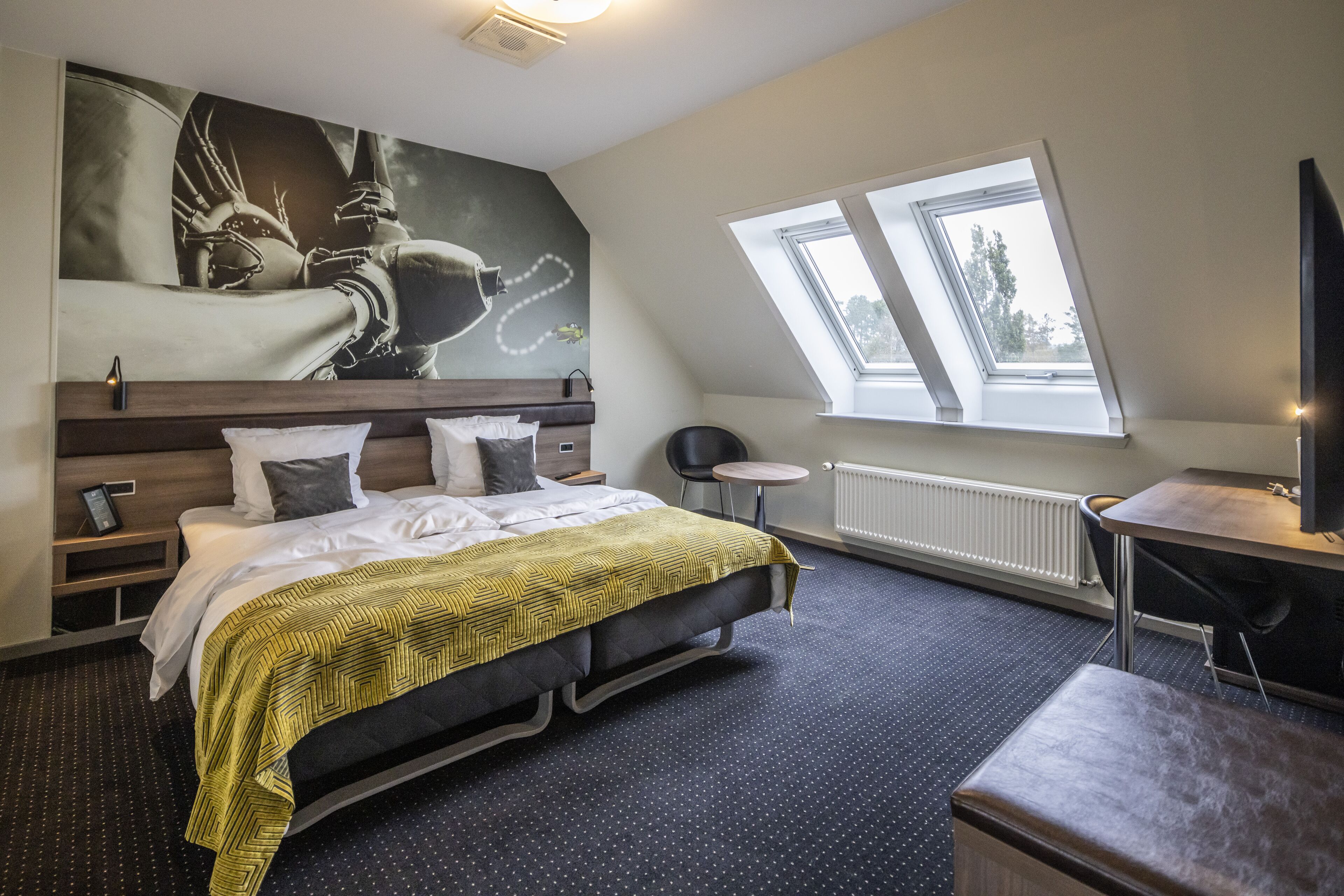 A modern hotel room with a large bed, a desk, and a skylight.