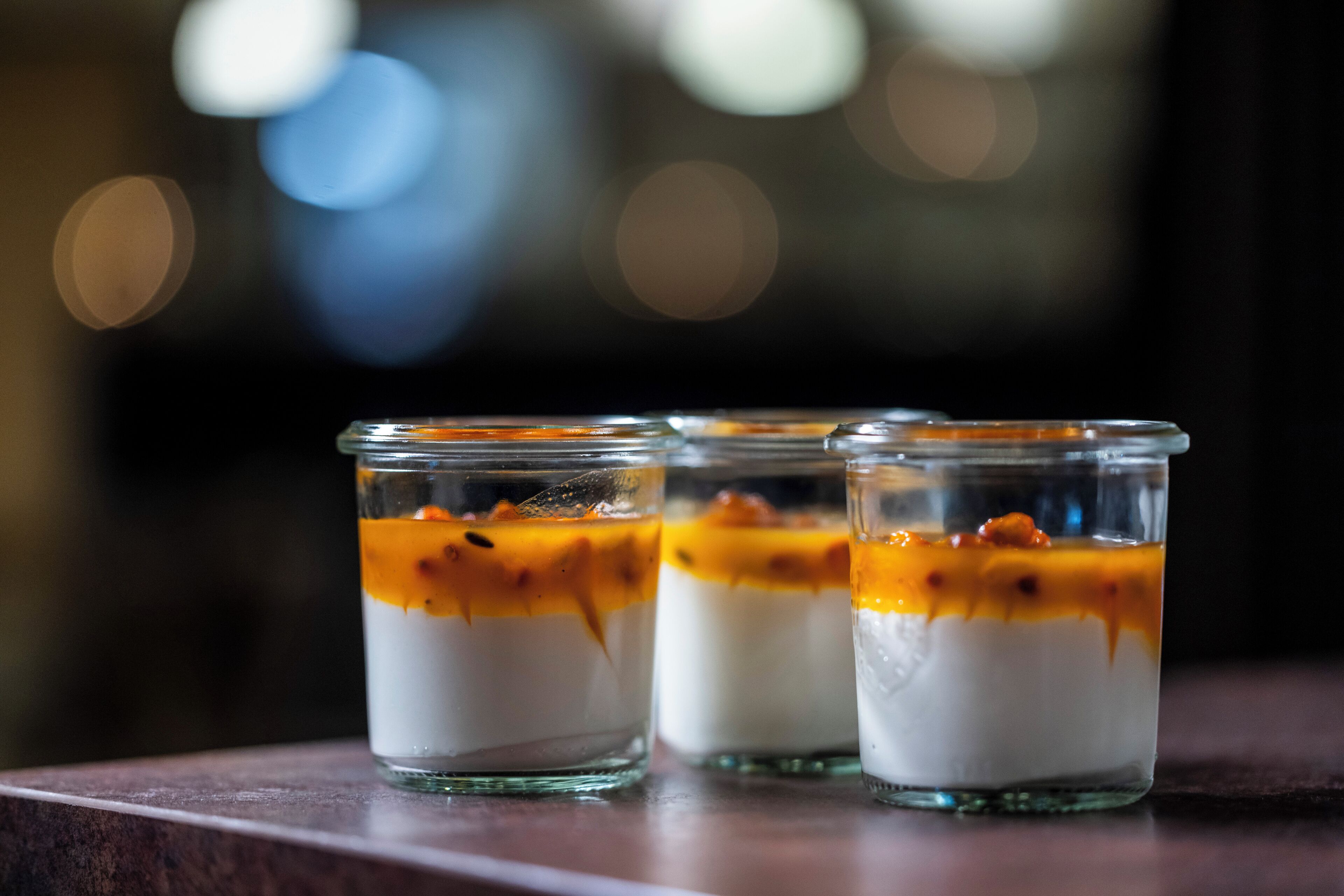 Tres vasos de vidrio transparentes con postre en capas y un chorrito de caramelo sobre una superficie de madera.