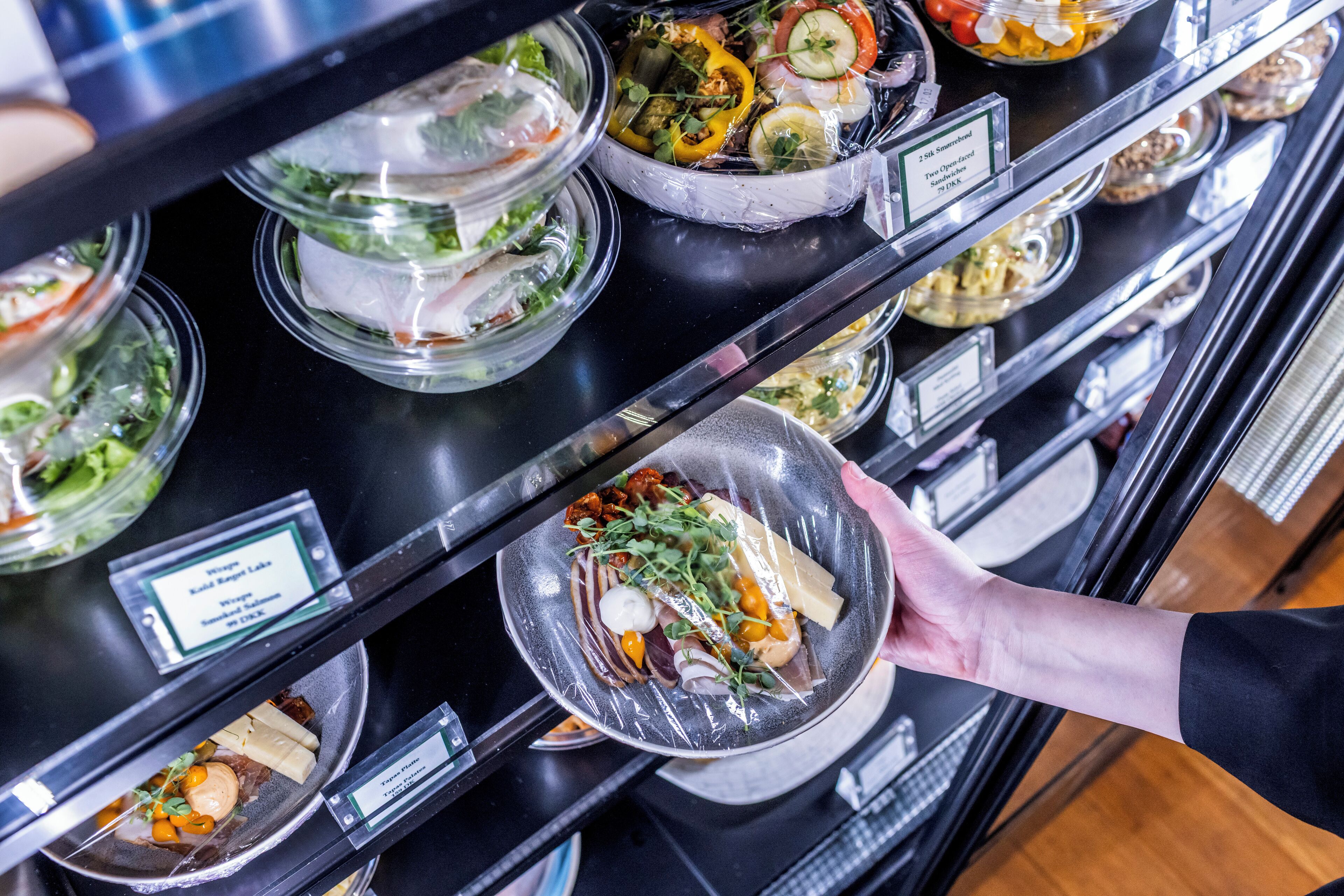 A buffet with various dishes displayed in clear containers, each labeled with the dish name and price.