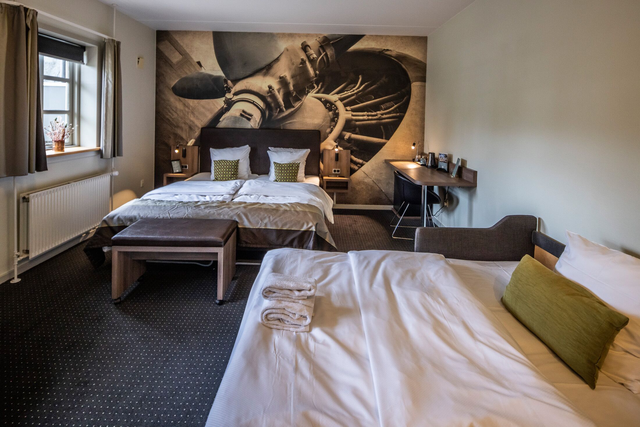 Ein Hotelzimmer mit zwei Betten, einer großen Wandmalerei, einem Schreibtisch und einem Fenster mit Vorhängen.