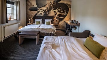 A hotel room with two beds, a large mural on the wall, a desk, and a window with curtains.
