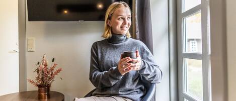 Una persona sentada junto a una ventana con vistas al exterior, sosteniendo una taza.