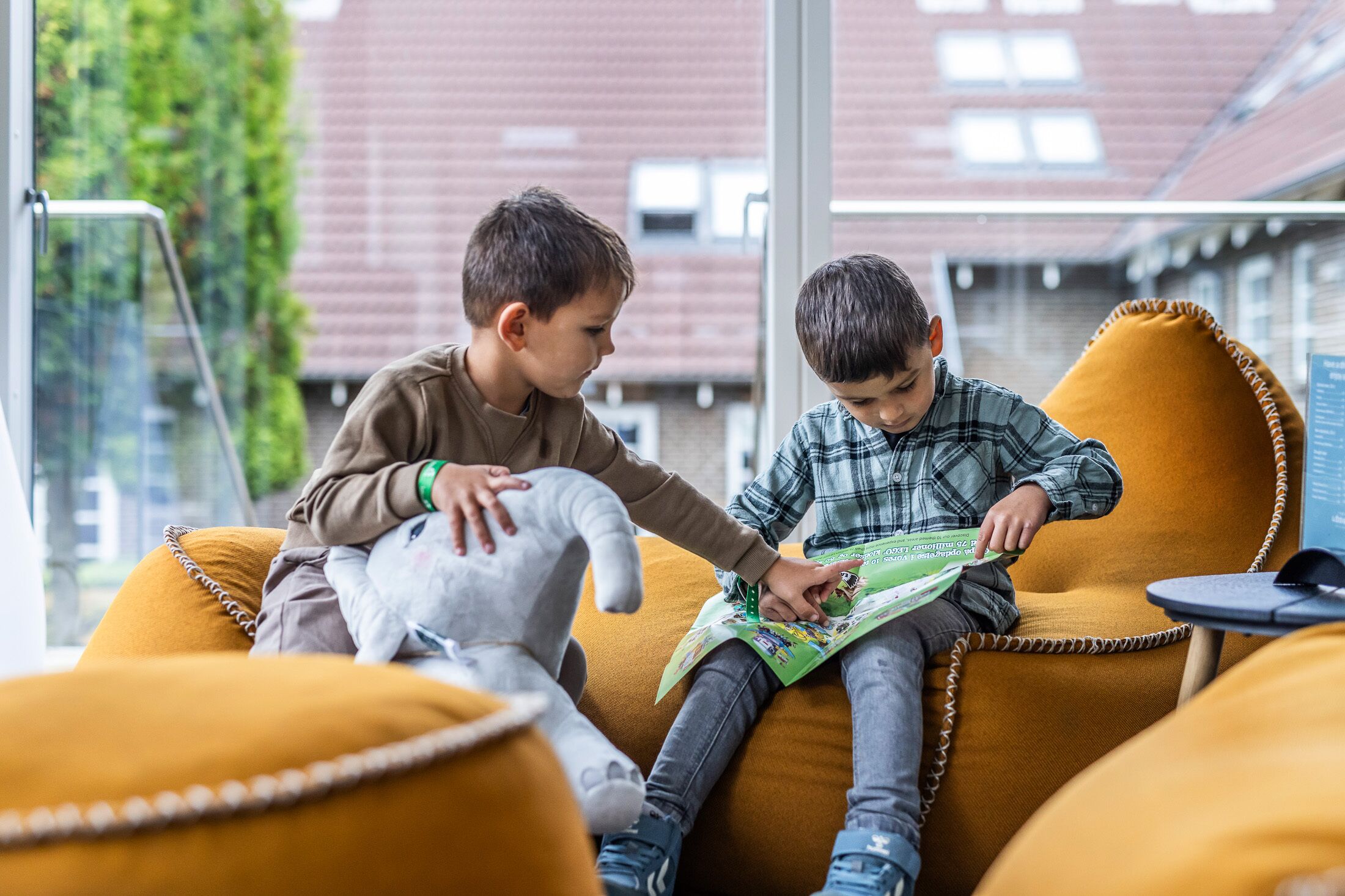Dos niños sentados en un sofá amarillo, leyendo un libro juntos.