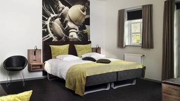 A modern hotel room with a large bed, a headboard with a unique design, a bedside table, a chair, and a window with curtains.