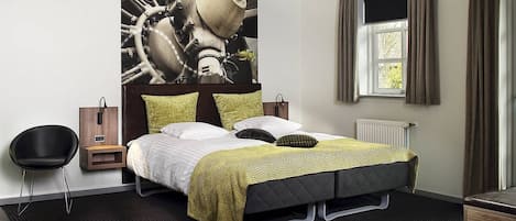 A modern hotel room with a large bed, a headboard with a unique design, a bedside table, a chair, and a window with curtains.