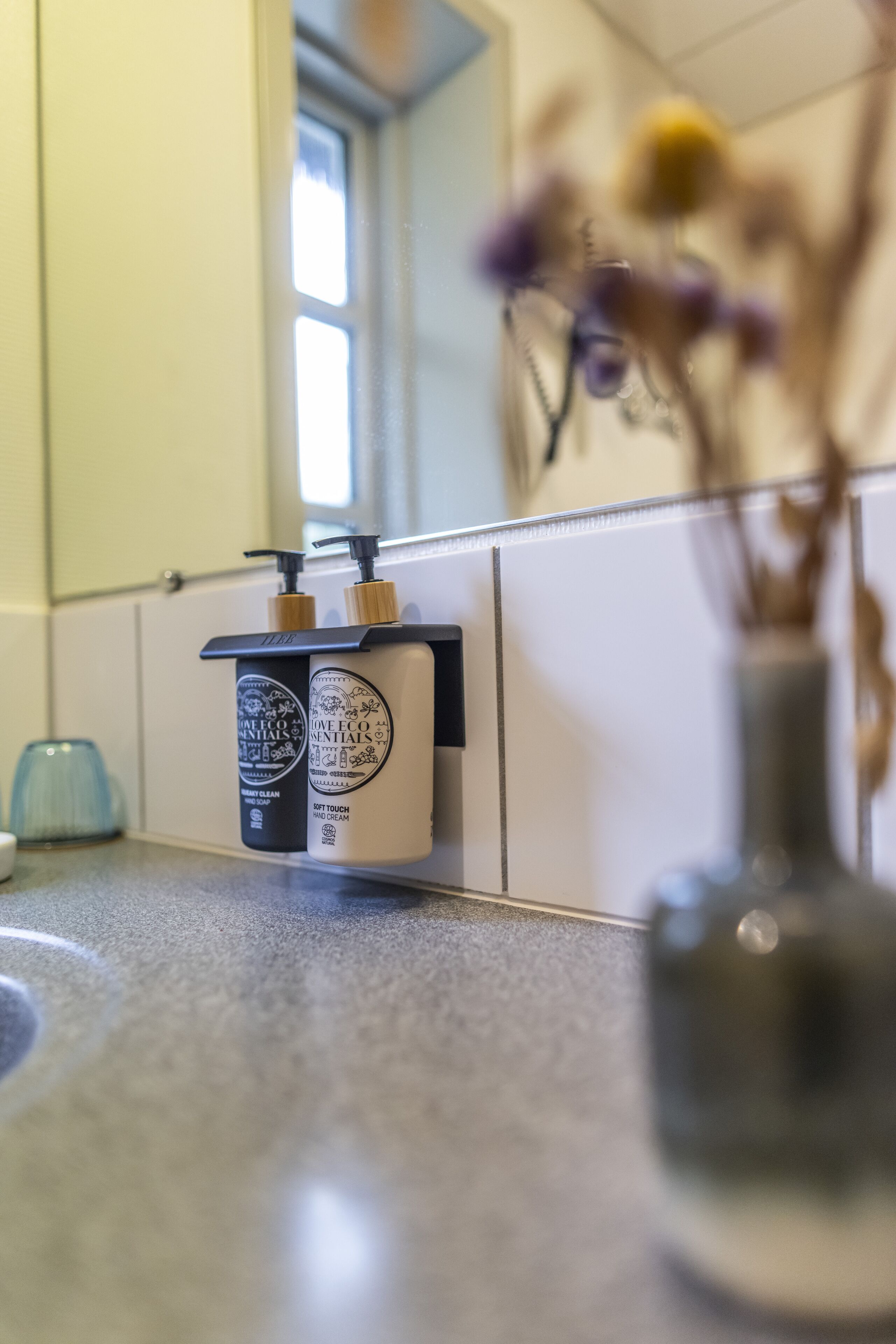 A bathroom with a mirror, a sink, and two bottles of hand cream on a shelf.