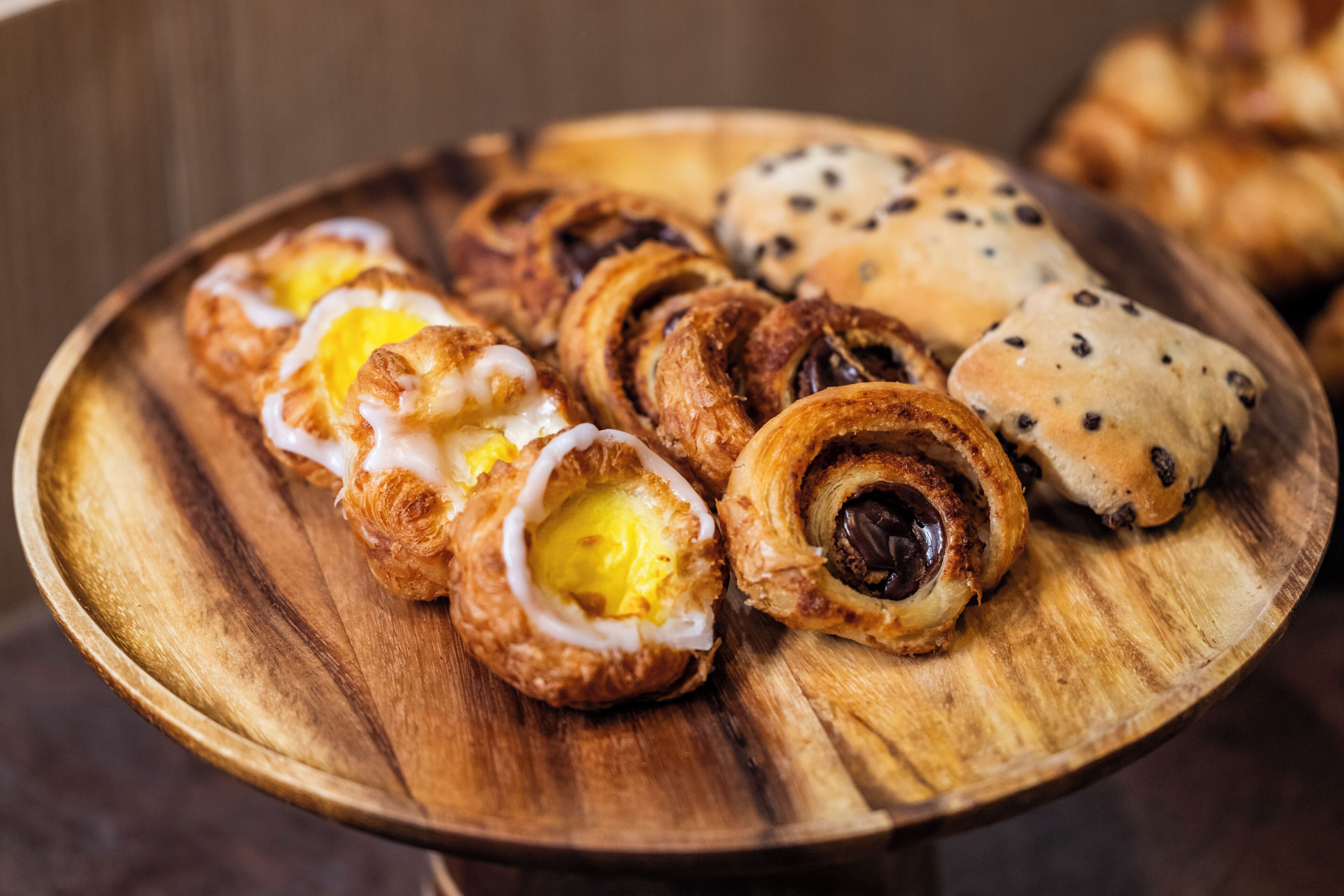 Una bandeja de madera con diversos pasteles, incluyendo croissants y bollos.