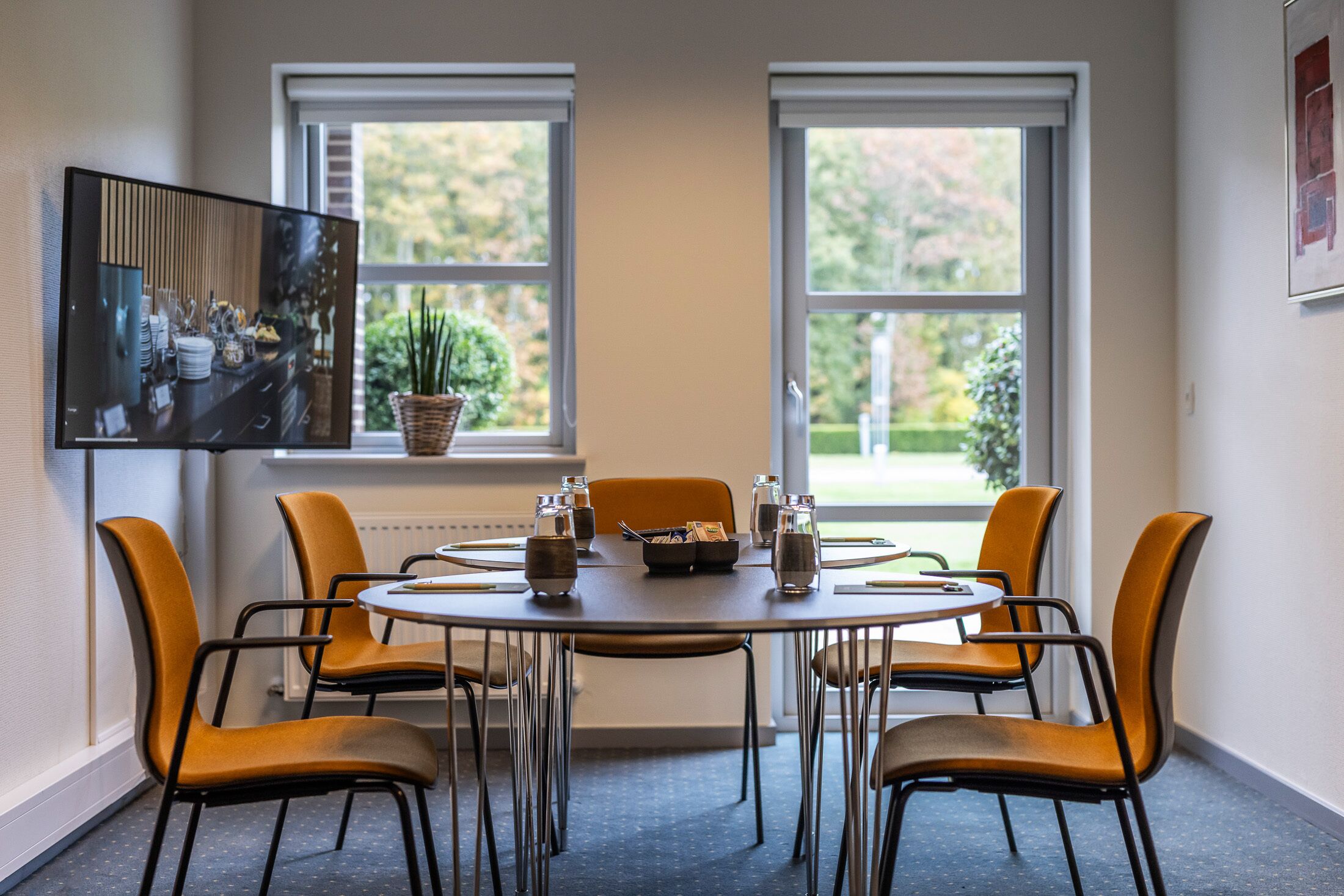 A dining area with a round table, four chairs, and a television mounted on the wall.