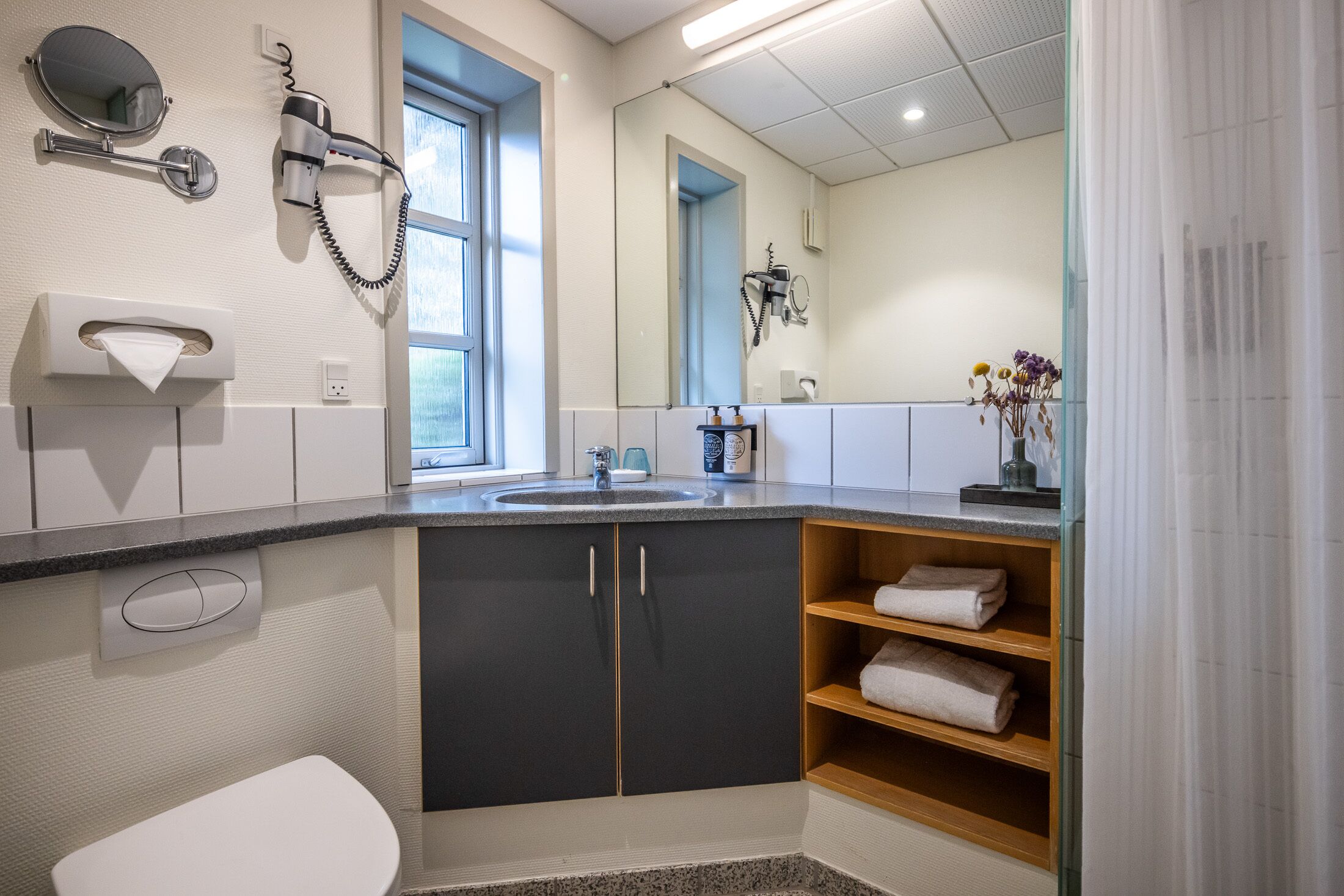 A modern bathroom with a sink, mirror, hairdryer, and towel rack.