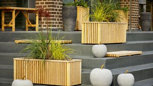 Outdoor wooden planters with plants and concrete apples on steps.