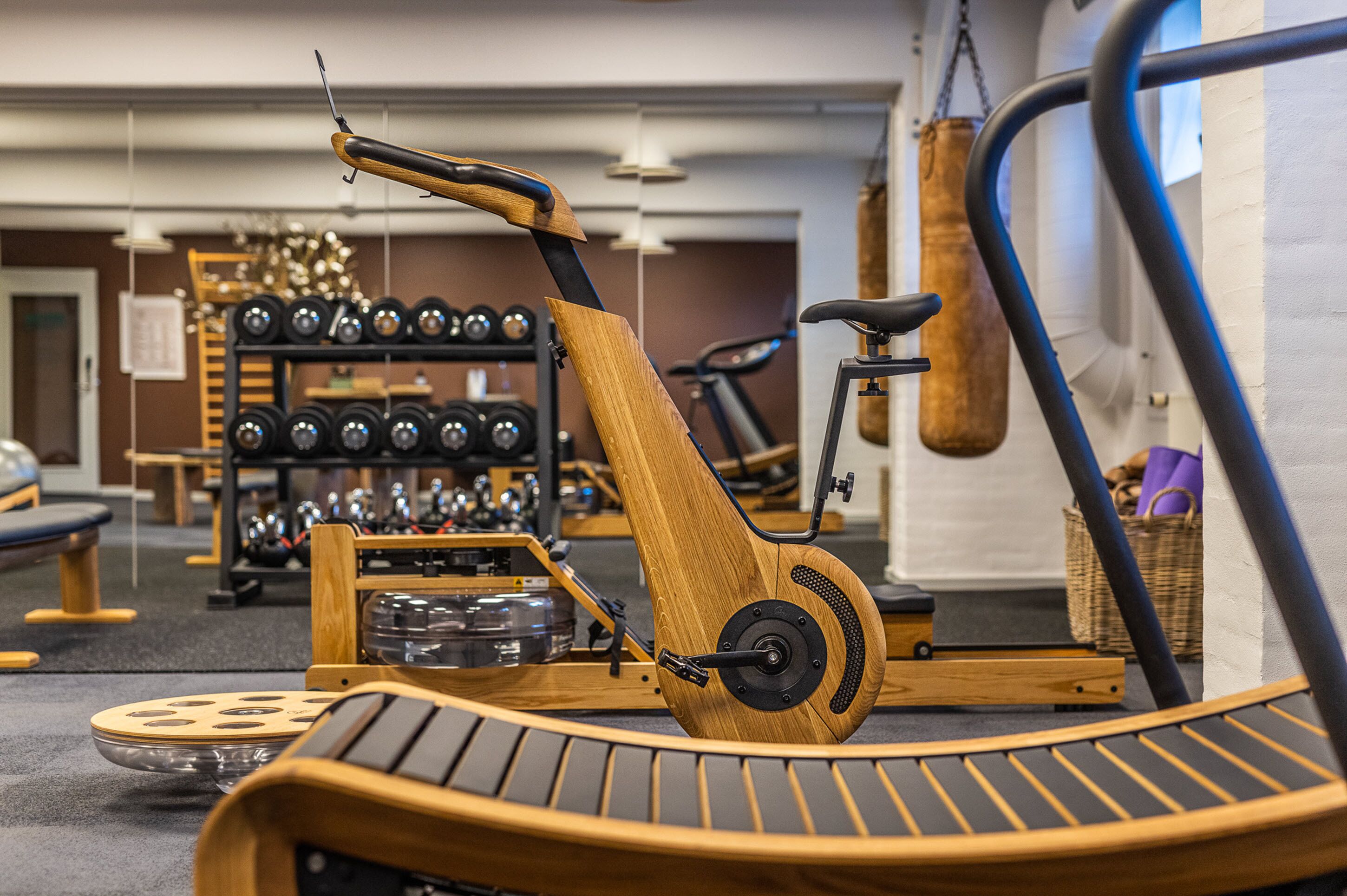 Un gimnasio con equipo de ejercicio que incluye una máquina de remo de madera, mancuernas y un saco de boxeo.